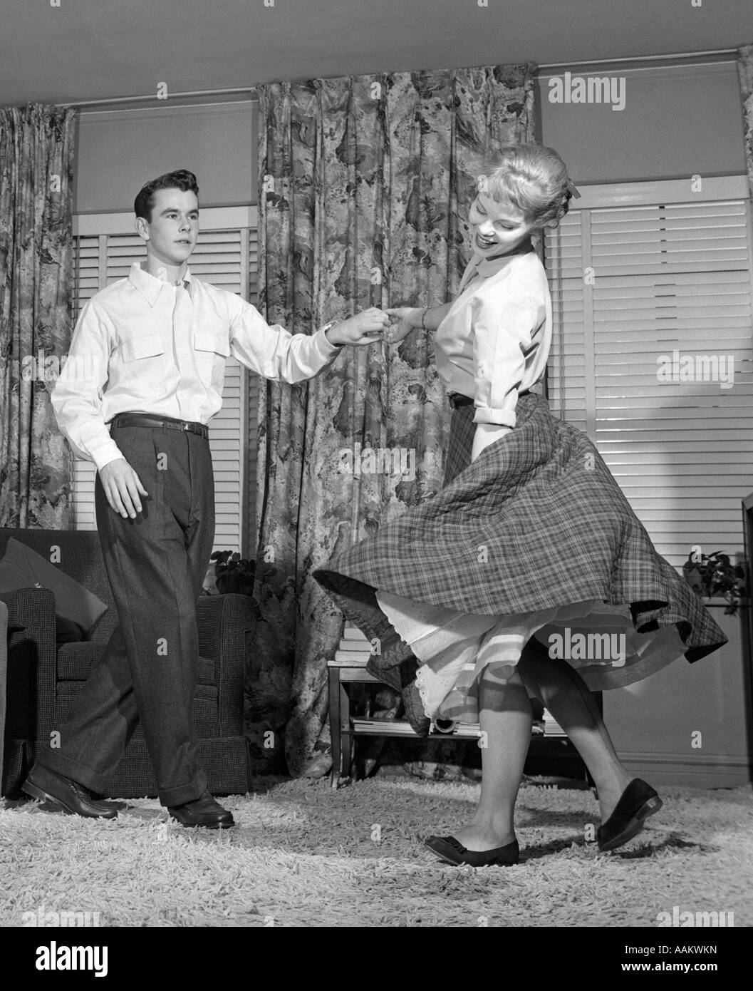 1950s TEENAGE COUPLE JITTERBUG DANCING TOGETHER IN LIVING ROOM Stock Photo