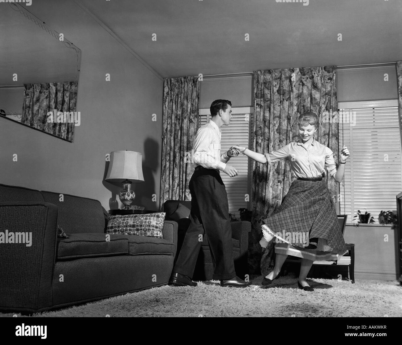 1950s TEEN COUPLE DOING JITTERBUG ROCK AND ROLL DANCE IN LIVING ROOM MAN WOMAN BOY GIRL Stock Photo