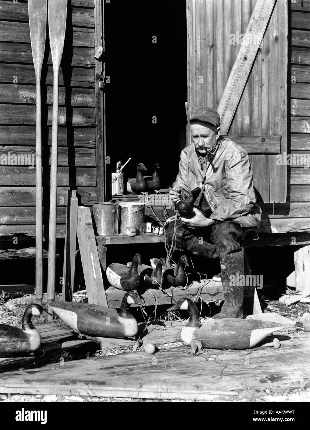 1930s 1940s SENIOR MAN SITTING ON STAIRS TO HUNTING SHACK PAINTING WOOD CANADA GEESE DECOYS BARNEGAT BAY NEW JERSEY USA Stock Photo