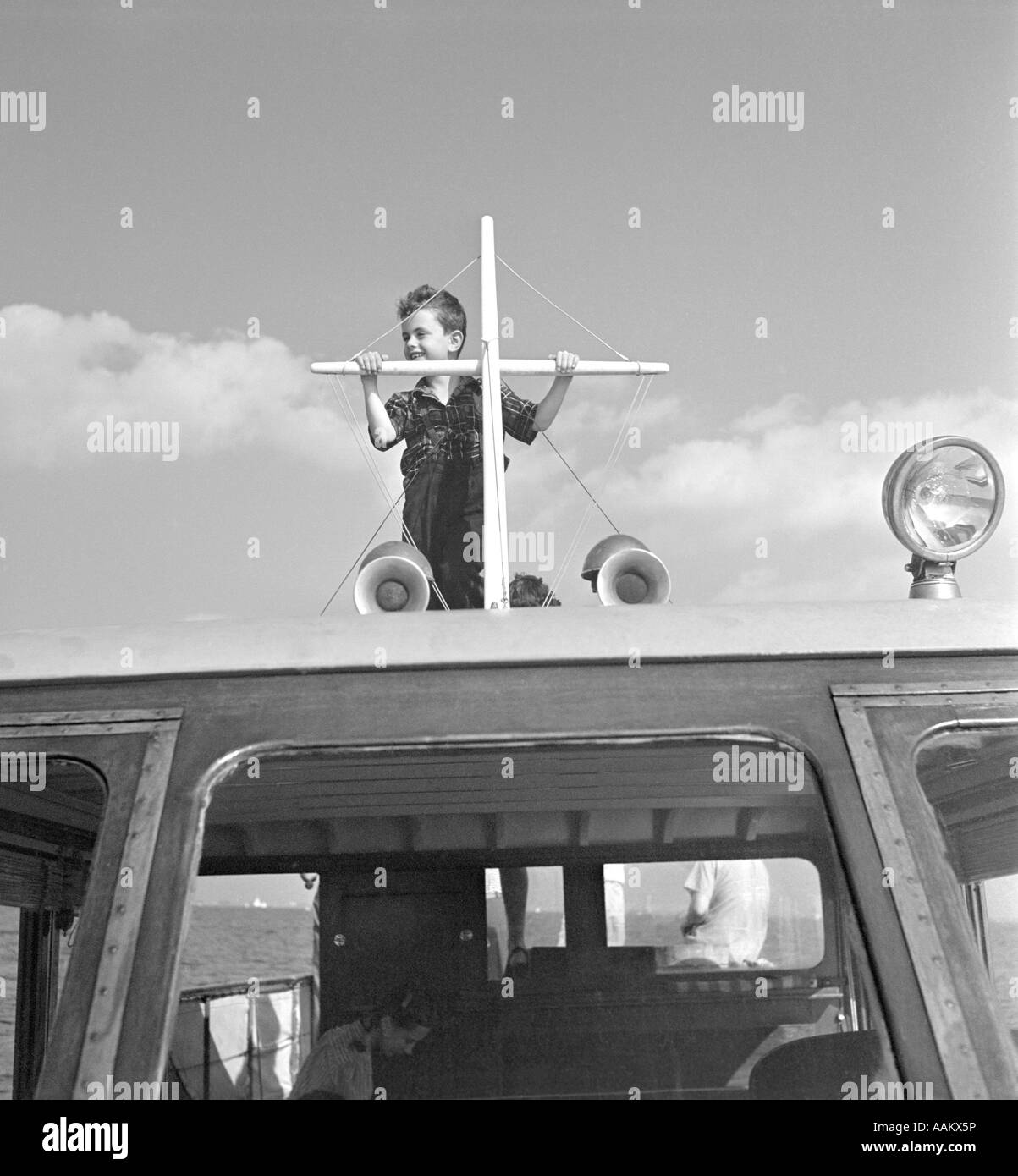 1940s BOY STANDING ON TOP OF MOTOR BOAT COCKPIT HOLDING ON TO SHORT MAST Stock Photo