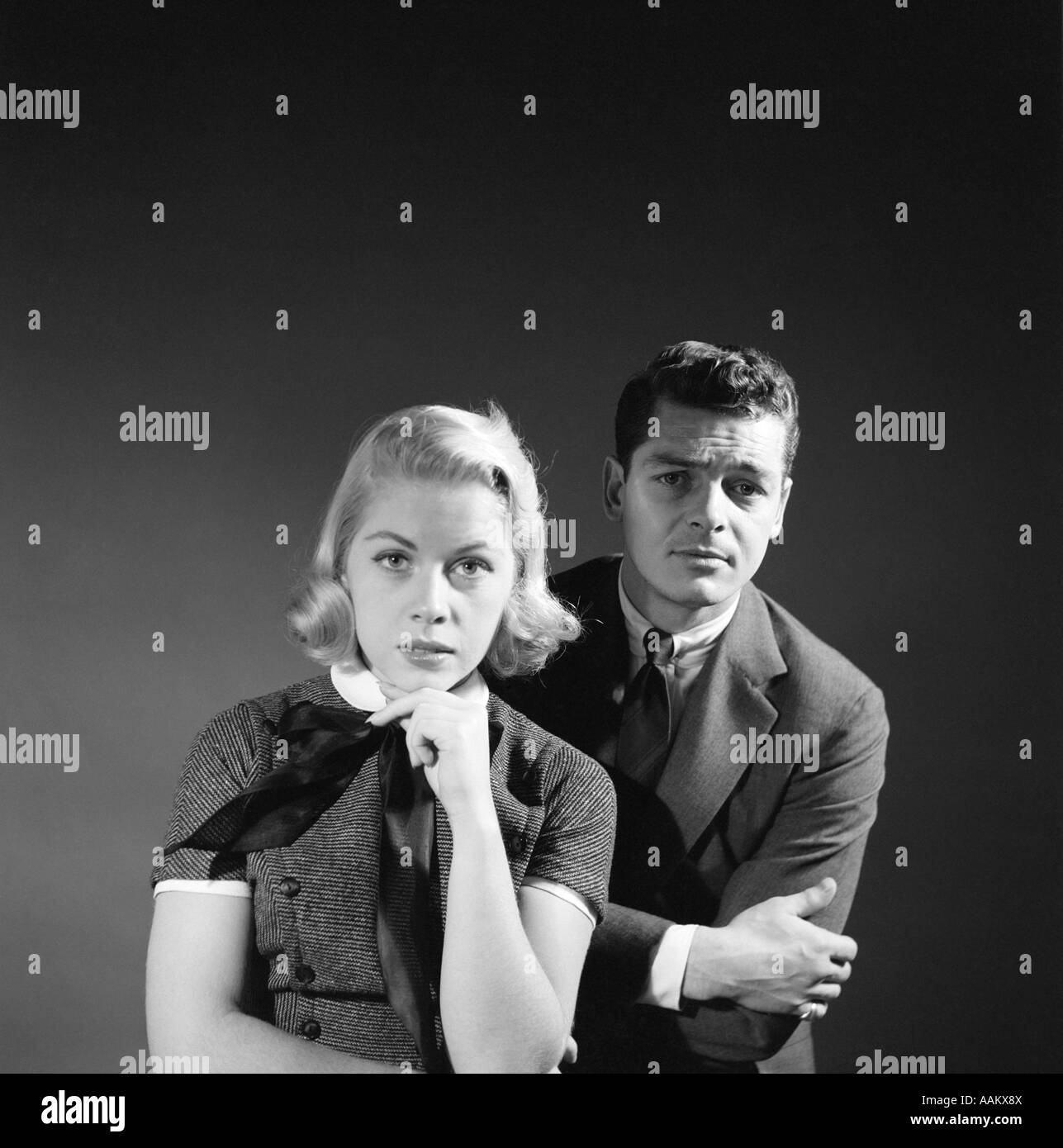 1950s COUPLE MAN BLOND WOMAN WITH SERIOUS PUZZLED EXPRESSIONS PORTRAIT LOOKING AT CAMERA Stock Photo