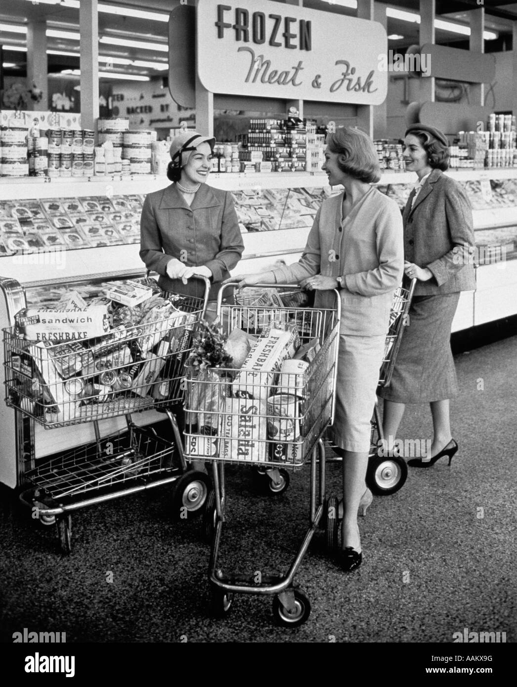 1950s THREE WOMEN PUSHING SHOPPING CARTS MEETING TALKING IN FROZEN FOOD AISLE OF SUPERMARKET Stock Photo