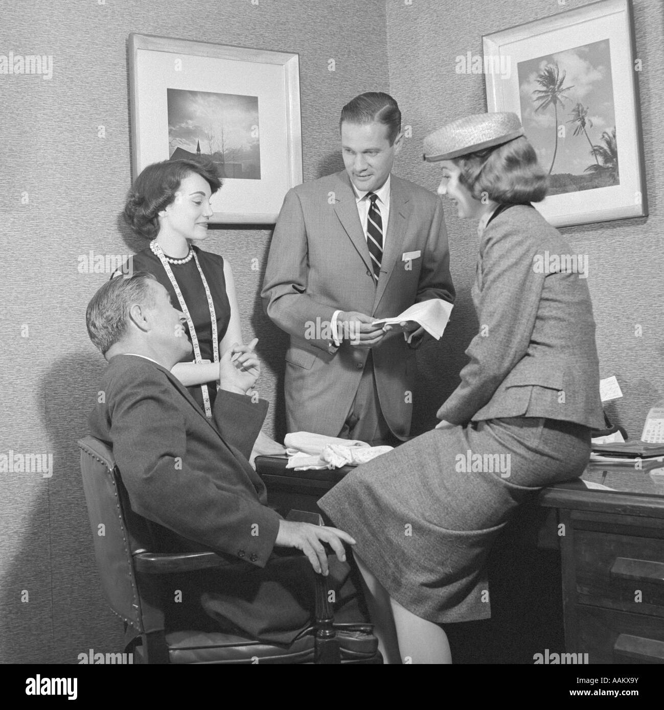 1950s TWO MEN AND TWO WOMEN DISCUSSING FABRIC SAMPLE AT DESK Stock Photo