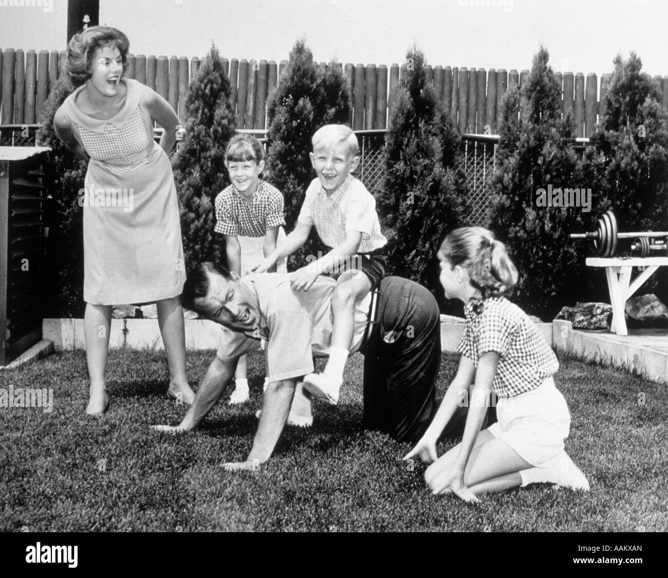 1960s FAMILY OF FIVE IN BACKYARD DAD GIVING PIGGYBACK RIDES TO CHILDREN Stock Photo