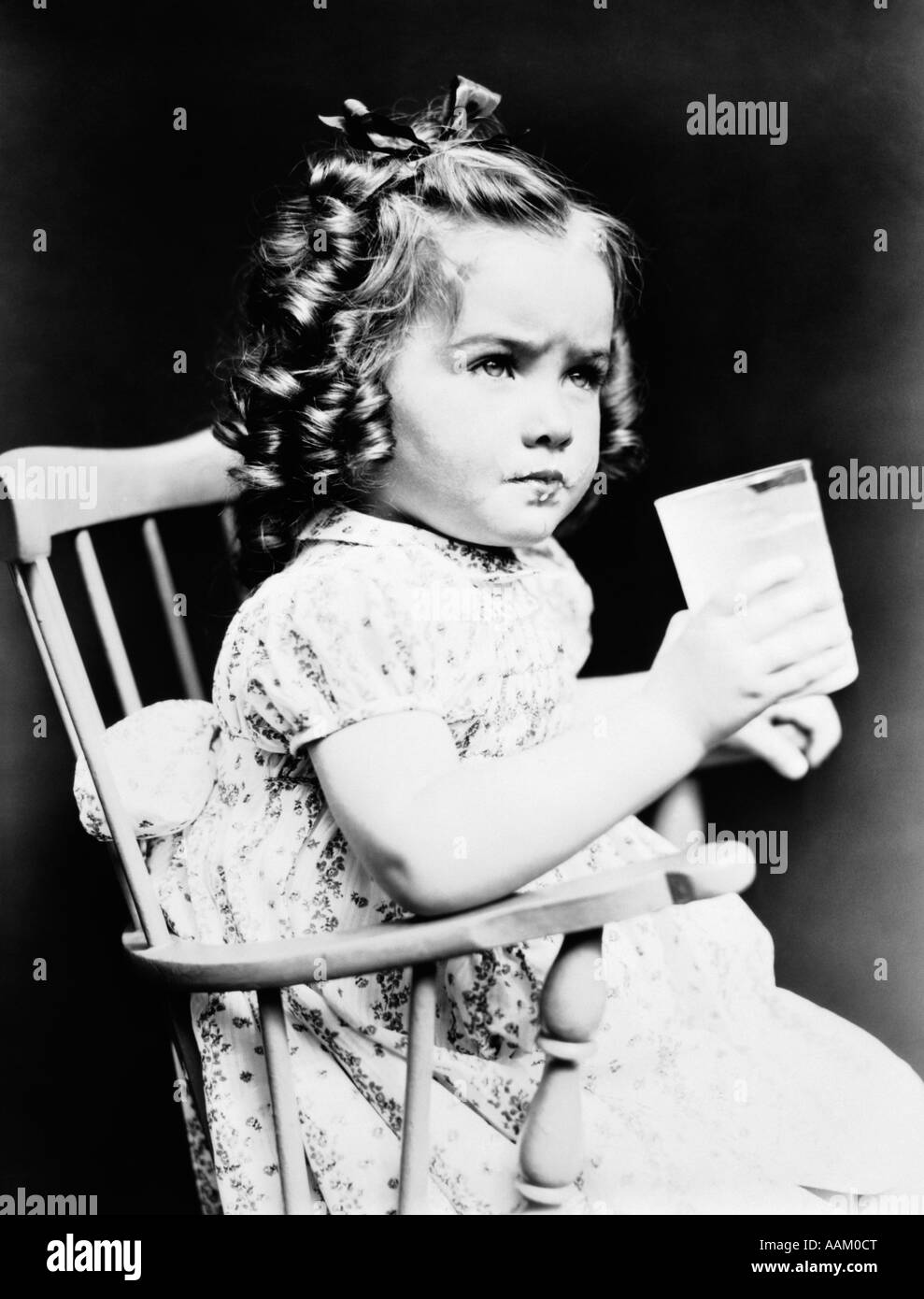 1930s CHILD GIRL SITTING IN HIGH CHAIR HOLDING GLASS OF MILK SERIOUS ...
