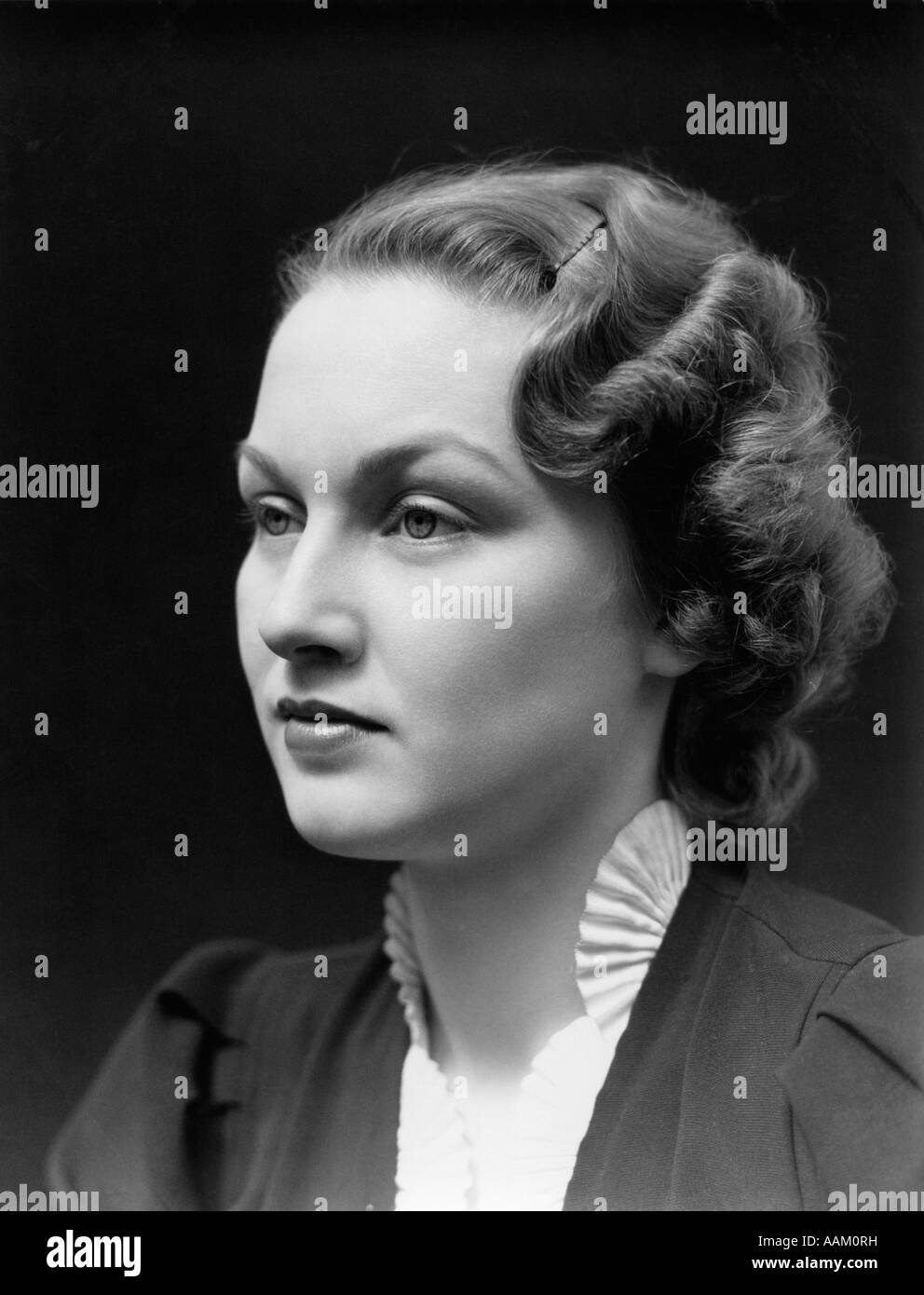 1930s PORTRAIT OF BRUNETTE WOMAN LOOKING OFF TO THE SIDE WITH A BLANK EXPRESSION WEARING A WHITE RUFFLED COLLAR Stock Photo