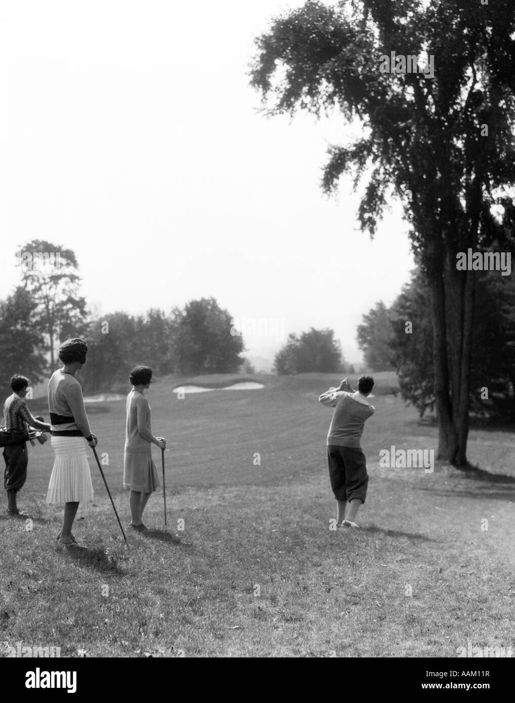 1920s 1930s MALE GOLFER IN THE ROUGH DRIVING DOWN FAIRWAY TWO WOMEN AND CADDY WATCHING Stock Photo