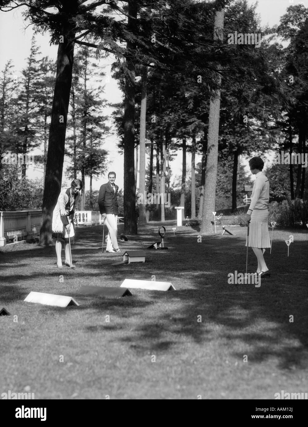1920s 1930s MAN TWO WOMEN PLAYING MINIATURE OBSTACLE GOLF COURSE Stock Photo