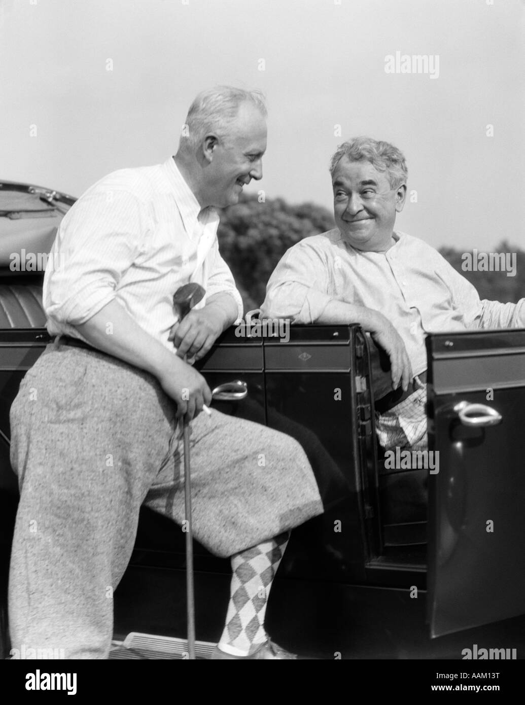 1920s 1930s ELDERLY MAN LEANING ON RUNNING BOARD OF CAR HOLDING GOLF CLUB & TALKING TO ANOTHER MAN SITTING IN THE CAR Stock Photo