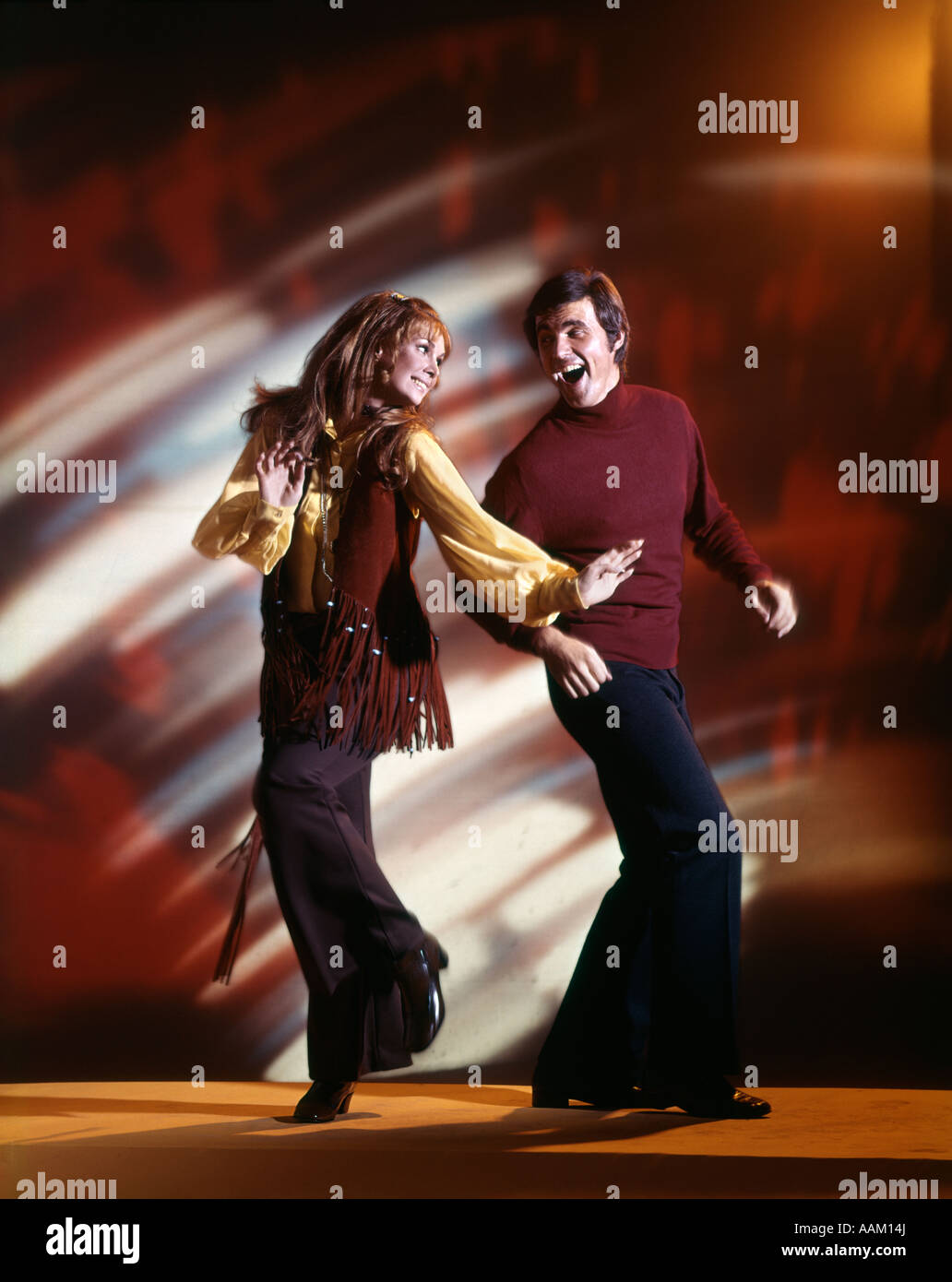 1960s MAN AND WOMAN DANCING IN DISCO CLUB WEARING BELL BOTTOM PANTS AND FRINGED VEST COUPLE FUN FAD NOSTALGIA Stock Photo