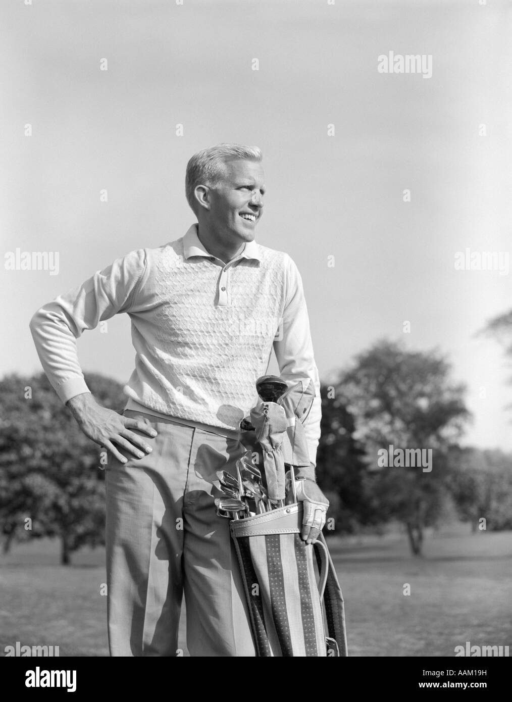 1960s SMILING BLOND MAN STANDING WITH GOLF BAG LOOKING DOWN FAIRWAY Stock Photo
