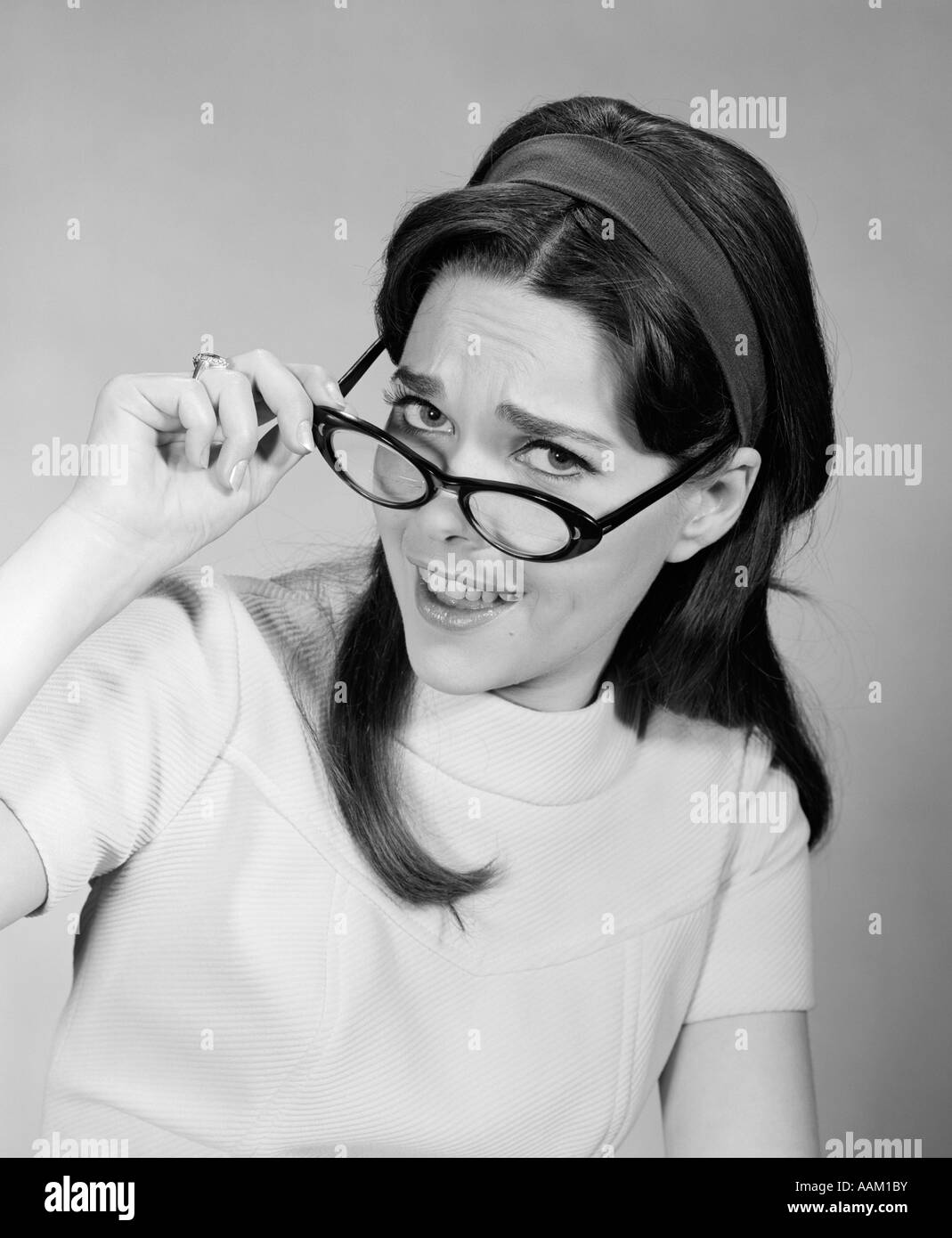 1960s WOMAN BRUNETTE LONG HAIR REMOVING PUTTING ON EYE GLASSES FUNNY FACIAL EXPRESSION LOOKING AT CAMERA Stock Photo