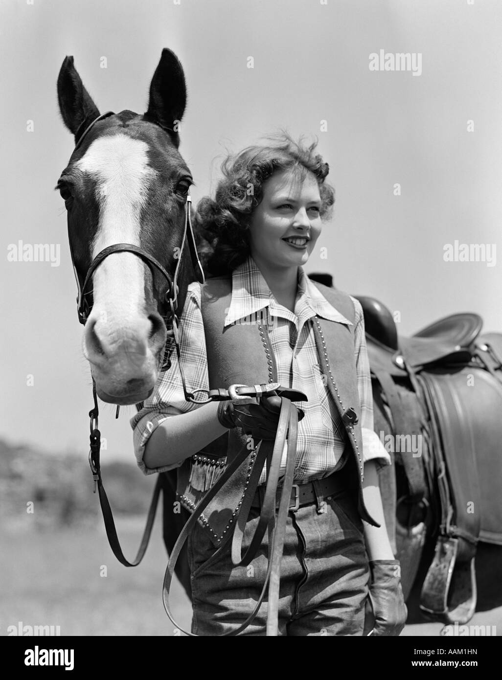 1940s SMILING TEENAGE GIRL IN STUDDED FRINGED WESTERN VEST WEARING LEATHER GLOVES HOLDING REINS OF HORSE Stock Photo