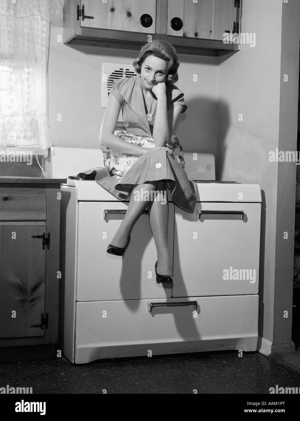 1950s 1960s WOMAN HOUSEWIFE SITTING ATOP ON STOVE ANGRY FRUSTRATED SERIOUS FACIAL EXPRESSION Stock Photo