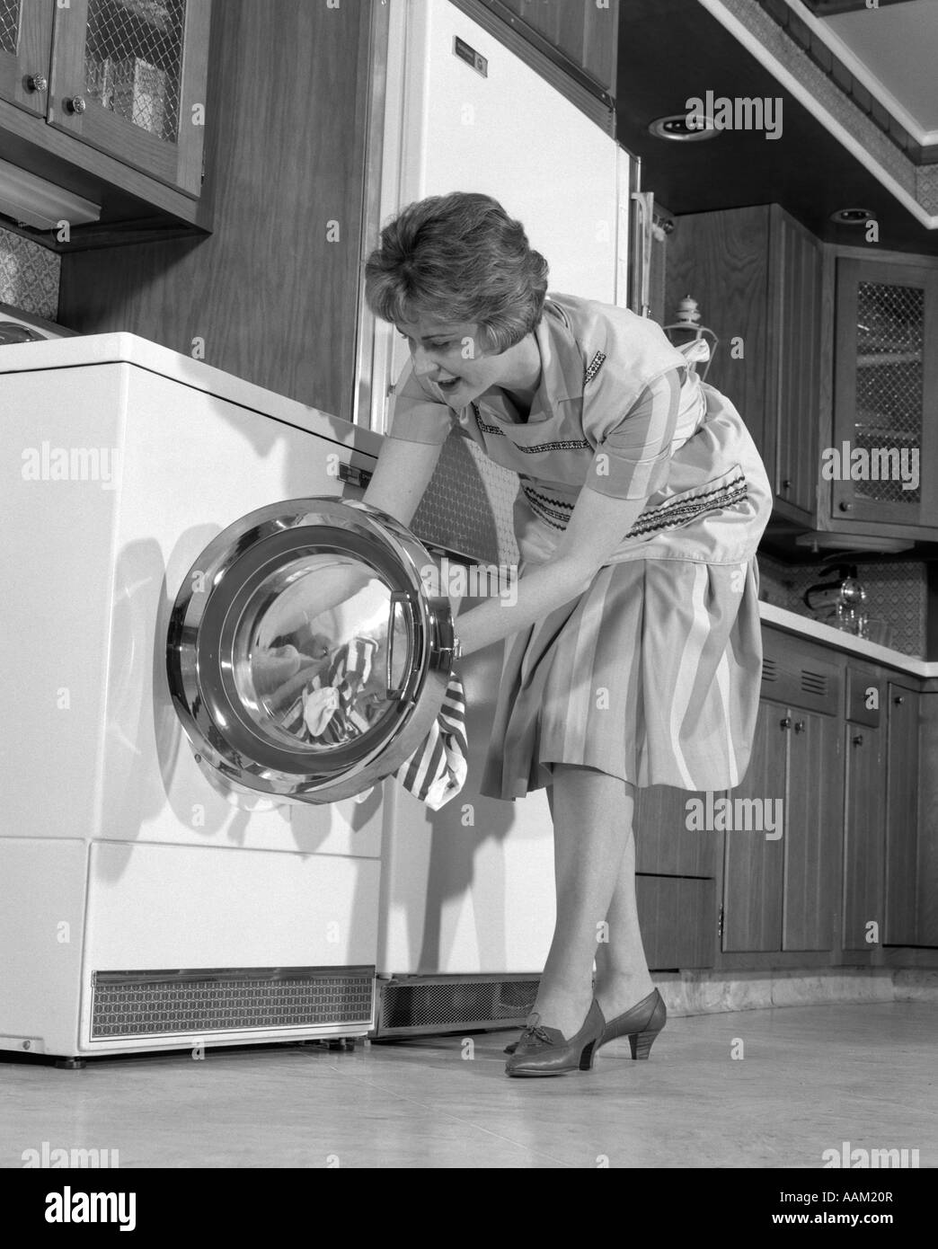 1960s HOUSEWIFE IN KITCHEN PUTTING LAUNDRY INTO WASHER Stock Photo
