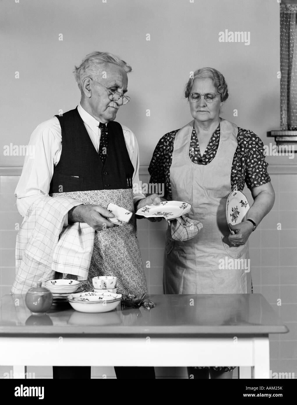 1940s 1950s ELDERLY COUPLE MAN WOMAN IN KITCHEN AT TABLE HOLDING DISHES ...