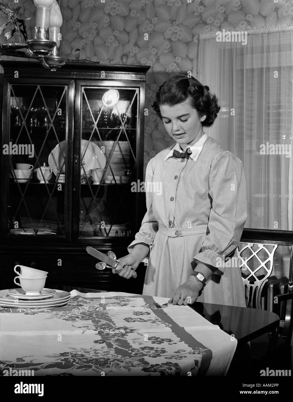 1950s TEEN GIRL SETTING THE TABLE IN DINING ROOM DOING HER HOUSEHOLD CHORE Stock Photo