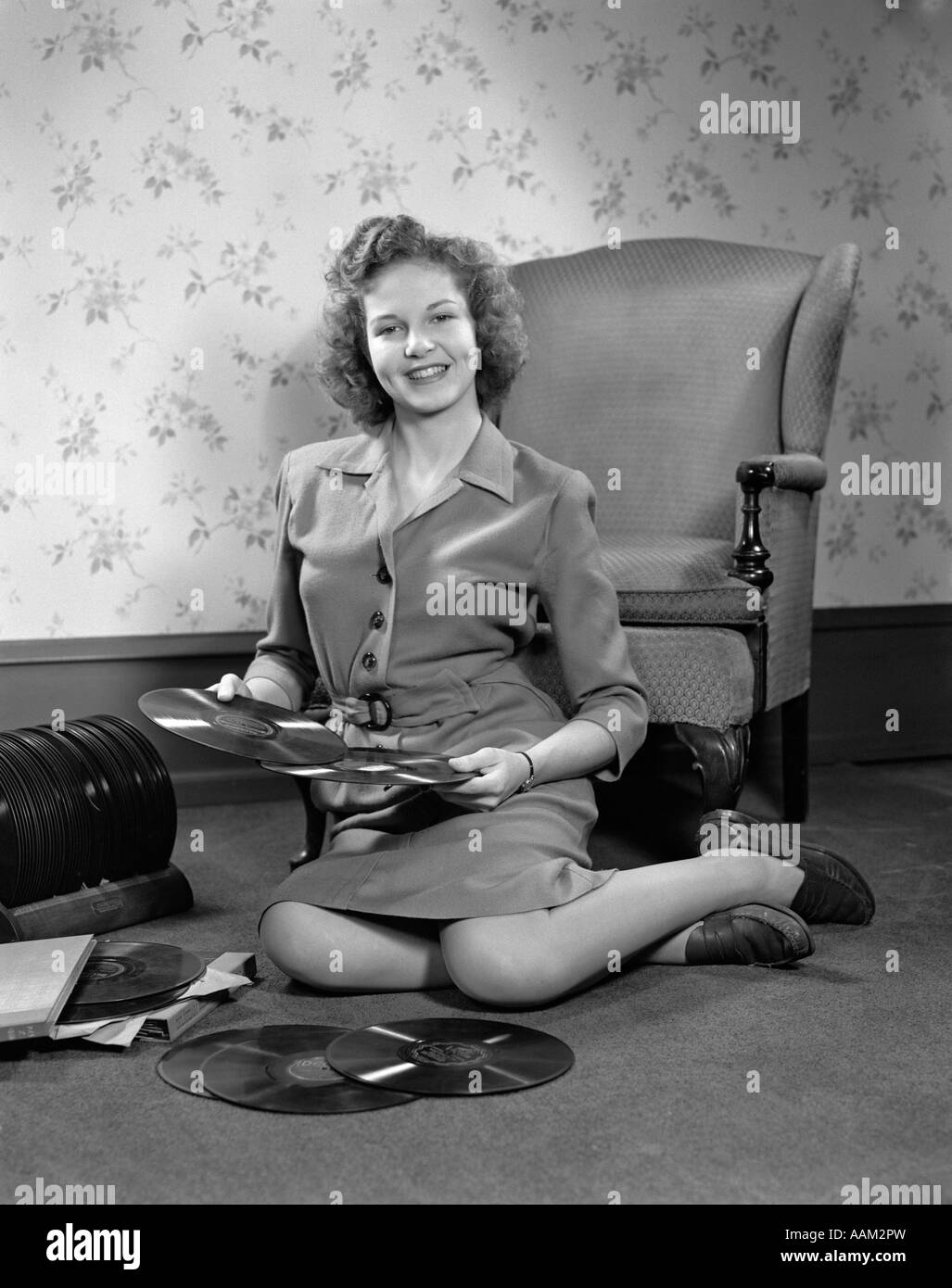 1940s YOUNG WOMAN TEEN SITTING ON FLOOR BY CHAIR HOLDING SORTING 78 RPM PHONOGRAPH RECORDS Stock Photo