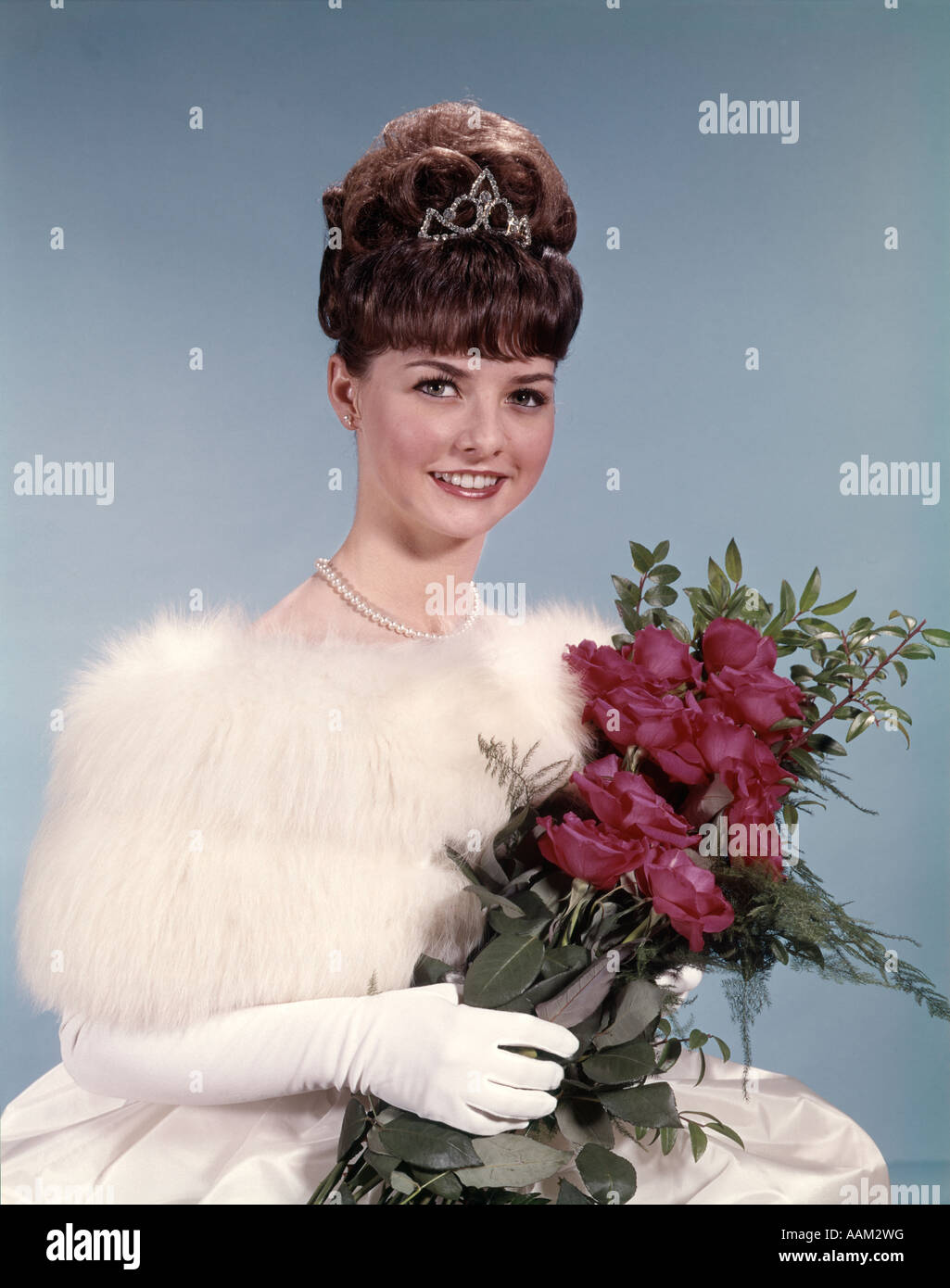 1960s YOUNG WOMAN WEARING CROWN WHITE FUR STOLE GLOVES HOLDING BOUQUET OF RED ROSES Stock Photo