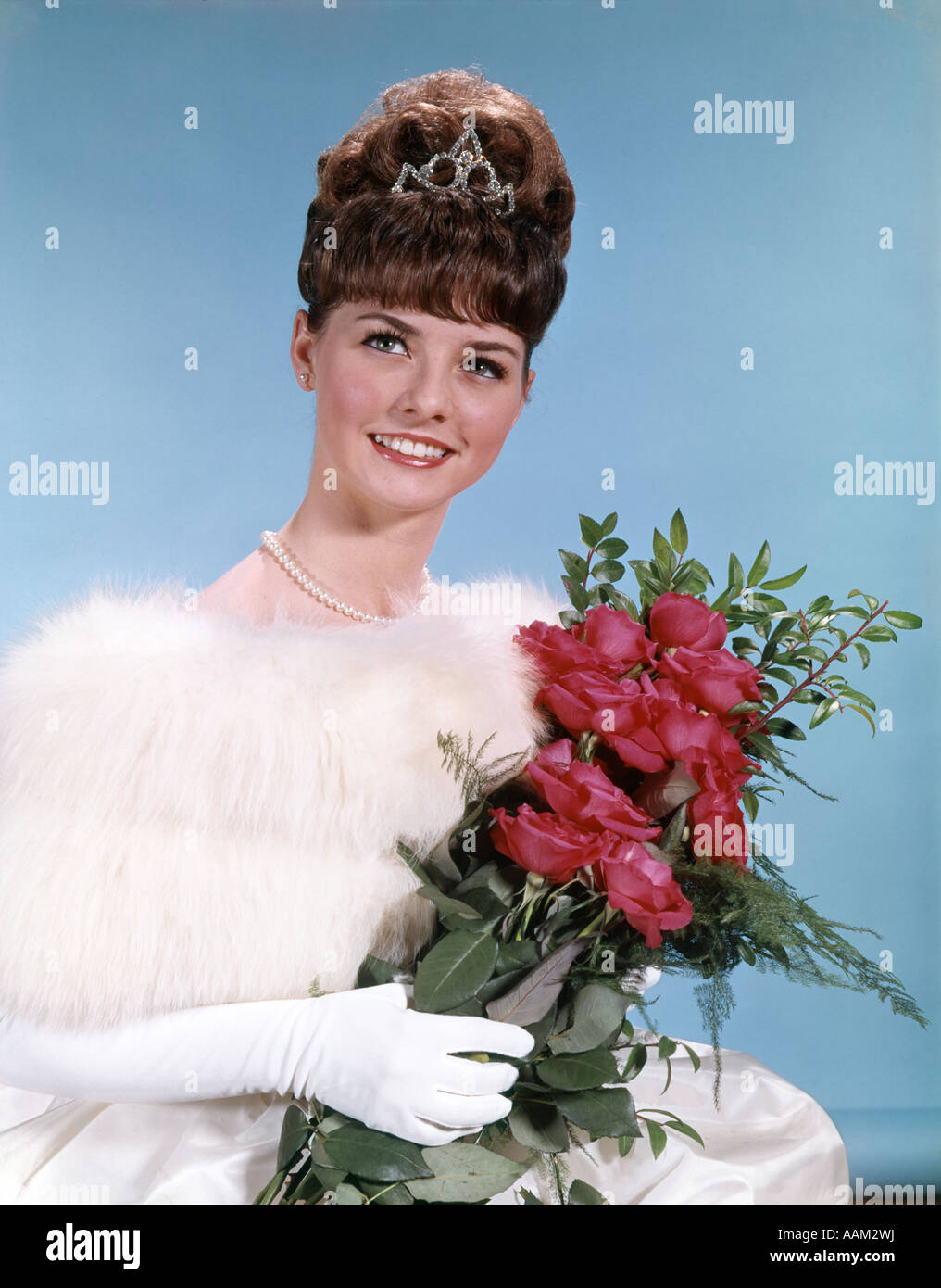 1960s YOUNG TEENAGE WOMAN IN FORMAL DRESS HOLDING BOUQUET ROSES BEE HIVE HAIRDO TIARA PROM BEAUTY QUEEN FASHION Stock Photo