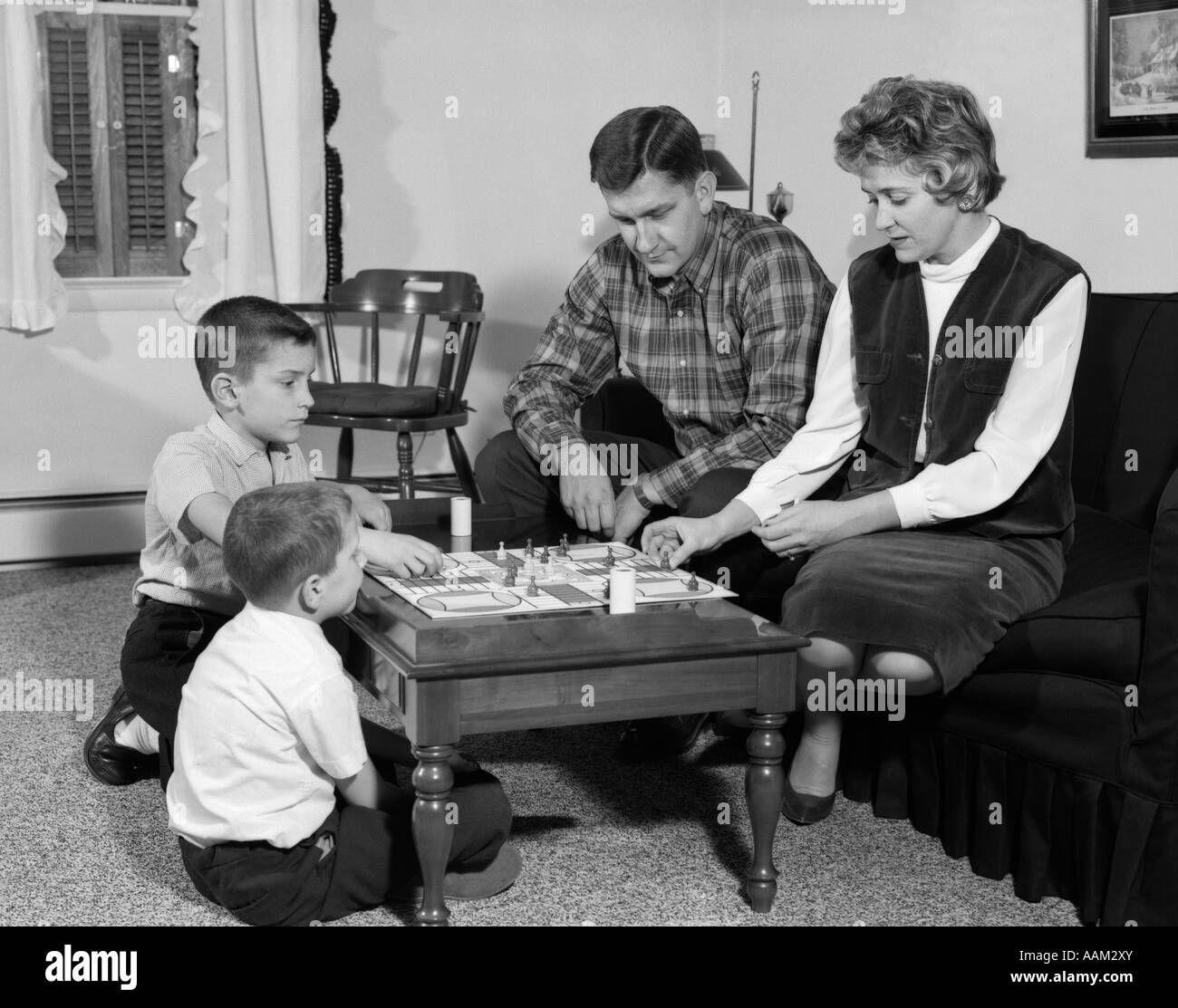 1960s MOTHER FATHER CHILDREN 2 KIDS BOYS PLAYING BOARD GAME PARCHEESI FAMILY FUN SOCIAL LIVING ROOM COFFEE TABLE 1960 Stock Photo