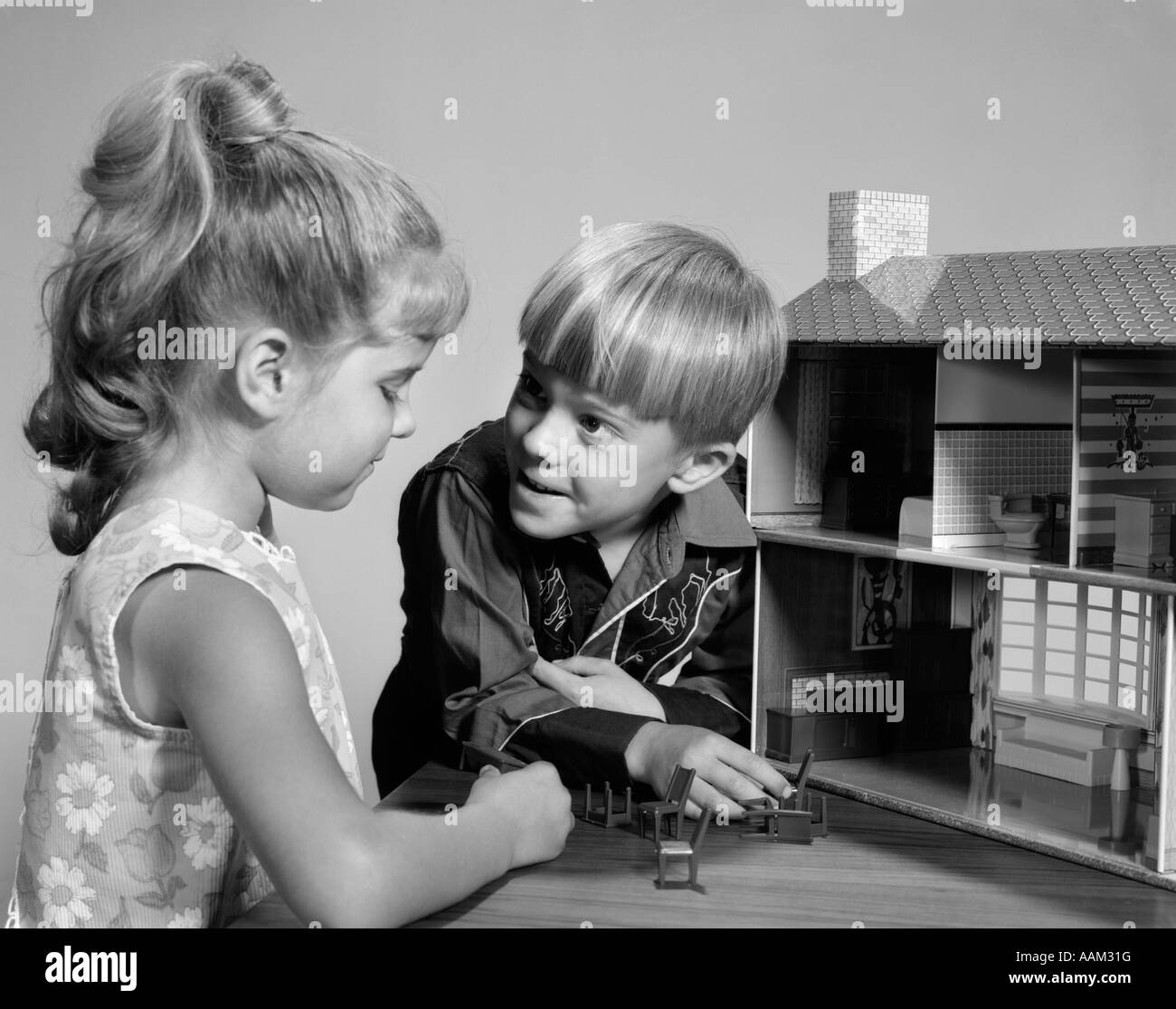 1960s TWO KIDS PLAYING WITH DOLL HOUSE TOY GIRL WITH PONY TAIL BOY IN WESTERN SHIRT Stock Photo