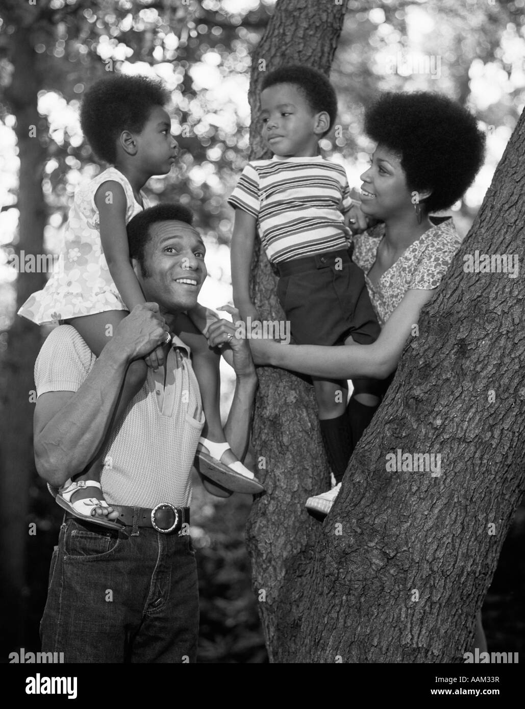 1970s AFRICAN AMERICAN FAMILY OUTDOORS BY TRUNK OF TREE MOTHER FATHER BOY GIRL Stock Photo