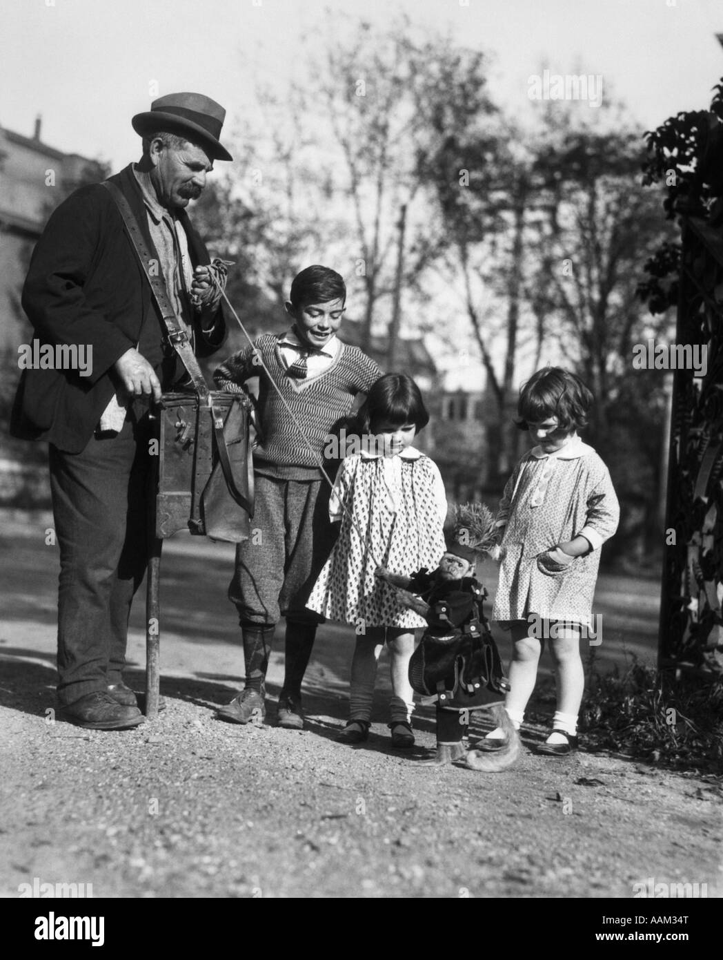 1920s GROUP OF THREE CHILDREN WATCHING ORGAN GRINDER'S MONKEY IN COSTUME STANDING ON HIND LEGS Stock Photo