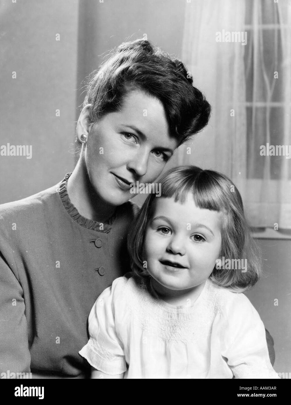 1940s 1950s PORTRAIT OF MOTHER WITH 3 YEAR OLD GIRL SITTING ON HER LAP BOTH FACING CAMERA Stock Photo