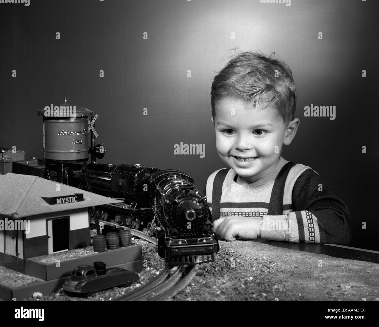 1950s BOY SMILING HAPPY PLAYING WITH MODEL TRAINS WITH A TOY RAILROAD STATION AND WATER TOWER Stock Photo