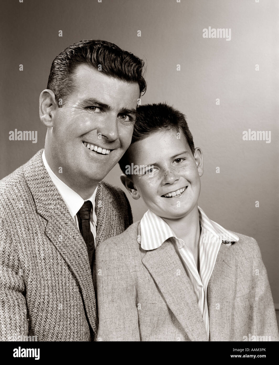 1950s STUDIO PORTRAIT SMILING MAN FATHER AND BOY SON SITTING TOGETHER LOOKING AT CAMERA Stock Photo