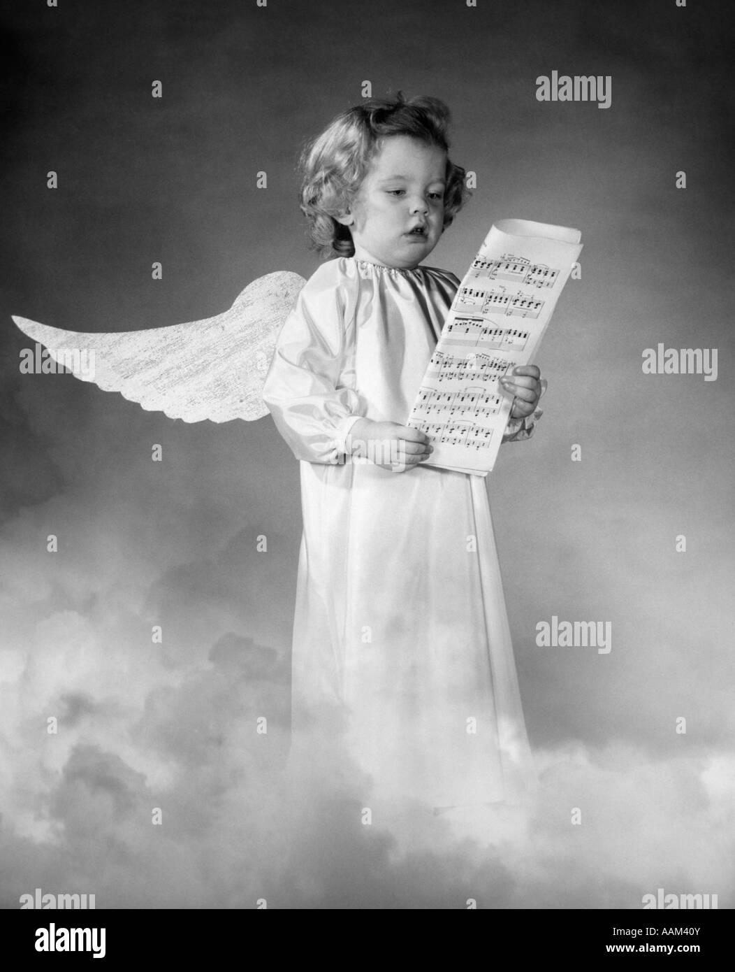 COMPOSITE PHOTO OF GIRL WITH WINGS STANDING IN CLOUDS SINGING WHILE HOLDING SHEET MUSIC WEARING A WHITE SMOCK Stock Photo