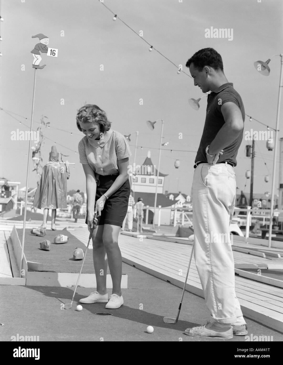 1960s TEENAGE COUPLE PLAYING MINIATURE GOLF Stock Photo
