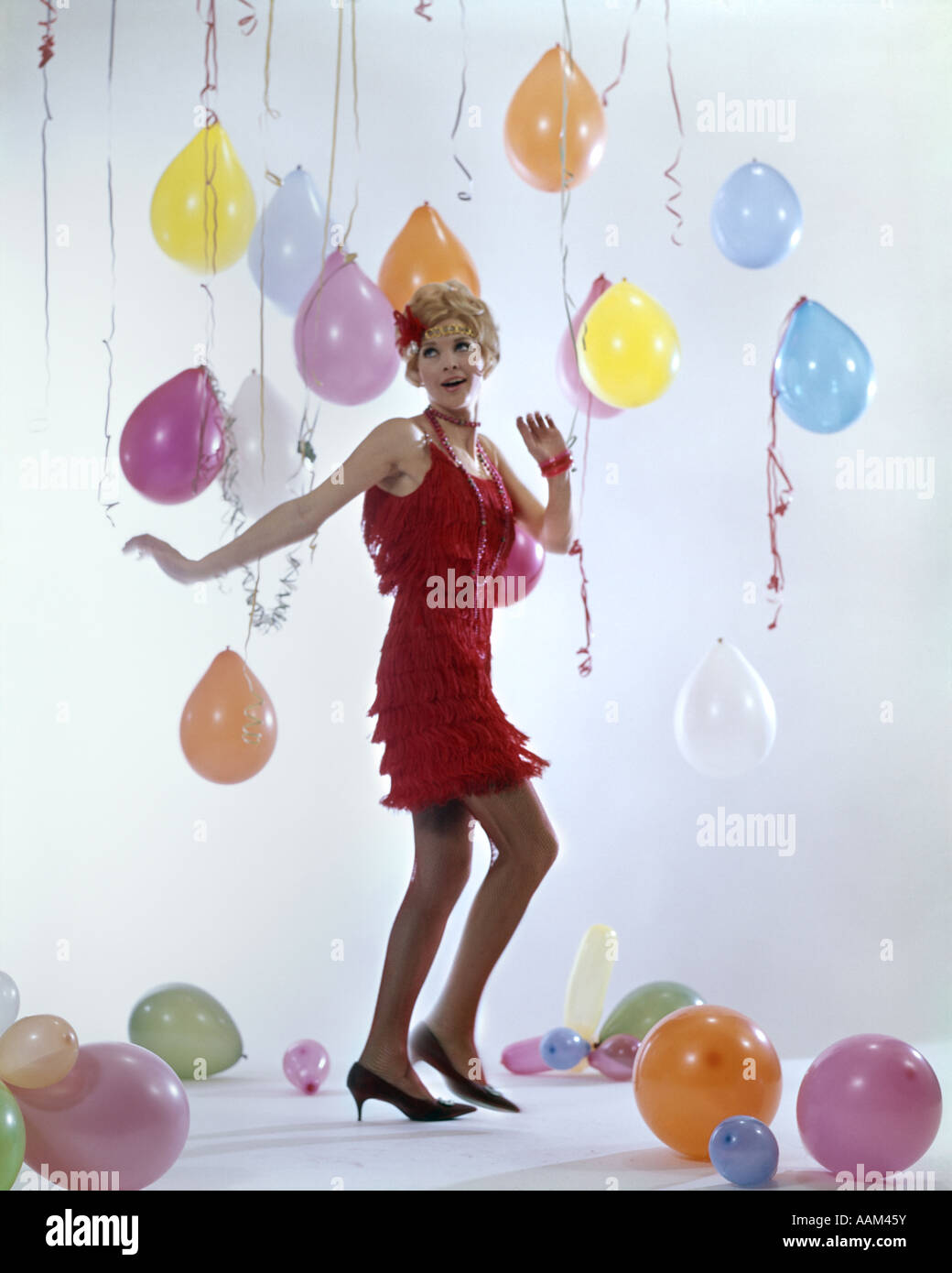 1970s WOMAN RED FRINGE 1920s FLAPPER DRESS DANCING CHARLESTON AMONG PARTY BALLOONS STREAMERS Stock Photo