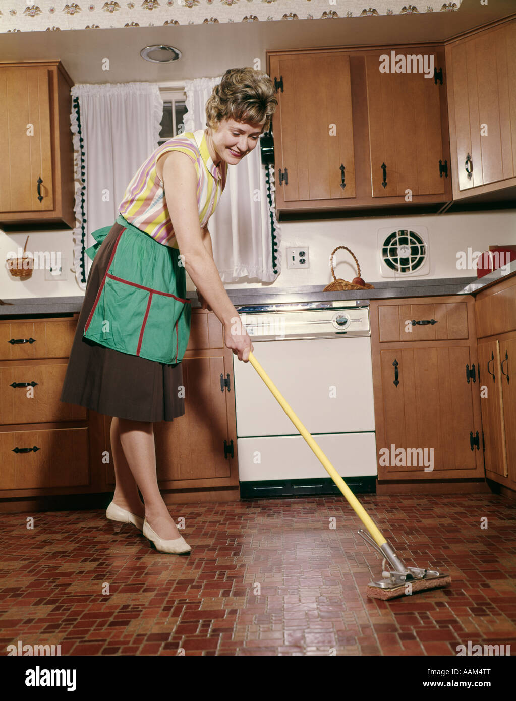 1960s Woman In Apron Cleaning Kitchen Floor With Sponge Mop Stock