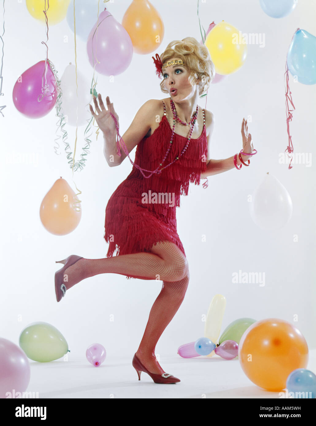 1970s WOMAN RED FRINGE 1920s FLAPPER DRESS DANCING CHARLESTON AMONG PARTY BALLOONS STREAMERS Stock Photo