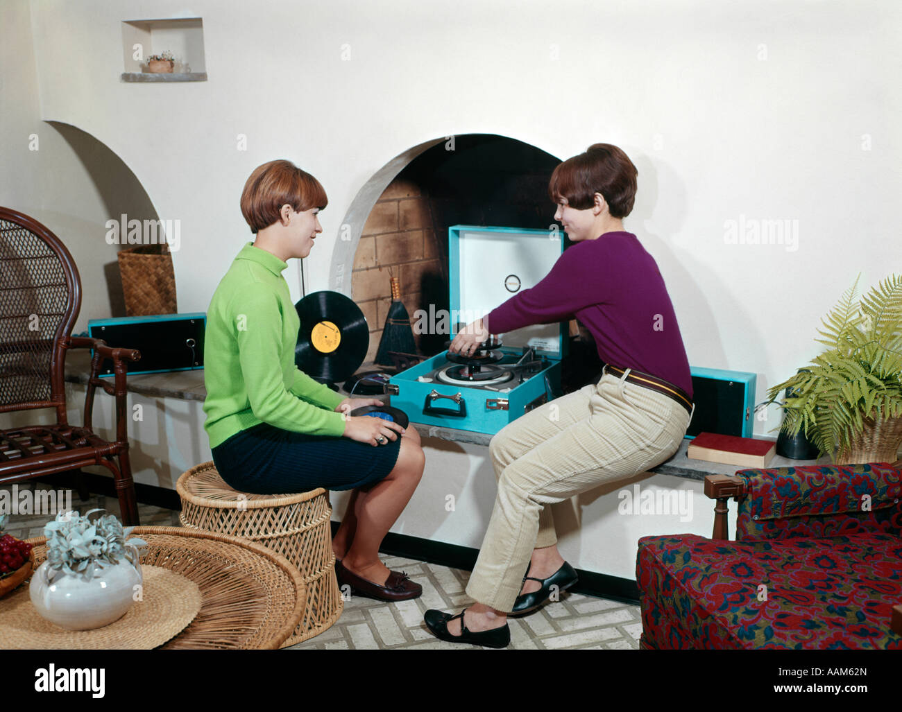 1960s TWO TEENAGED GIRLS PLAYING RECORDS ON PLAYER IN WALL NICHE IN LIVING ROOM Stock Photo