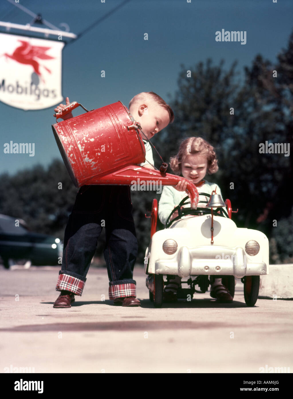 1950s LITTLE BOY PRETENDING TO SERVICE PEDDLE TOY CAR FIRE ENGINE FOR LITTLE GIRL Stock Photo