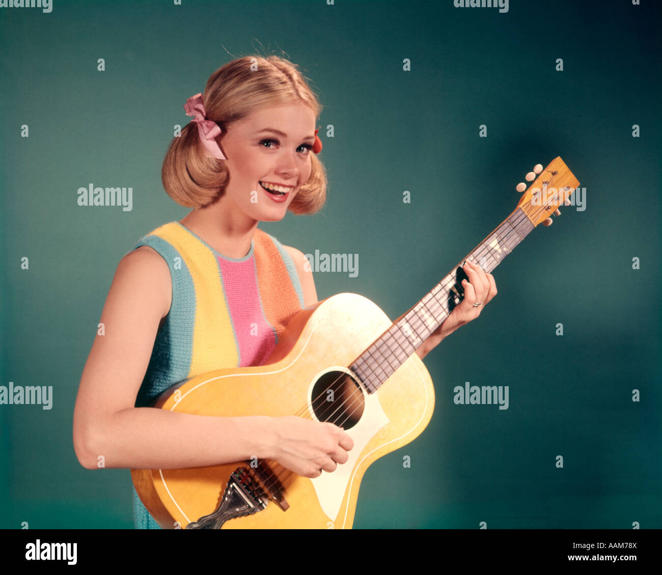 1960 1960s BLONDE YOUNG WOMAN PLAYING A GUITAR FOLKSINGER PERFORMER SMILING Stock Photo