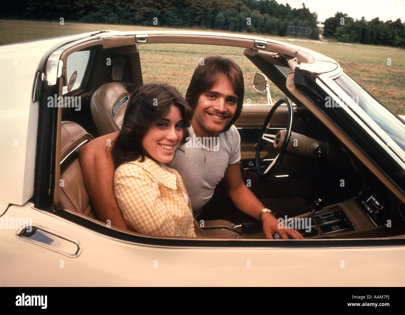 1970 1970s HAPPY SMILING COUPLE YOUNG MAN WOMAN SITTING COCKPIT CORVETTE CAR SPORTS CAR Stock Photo