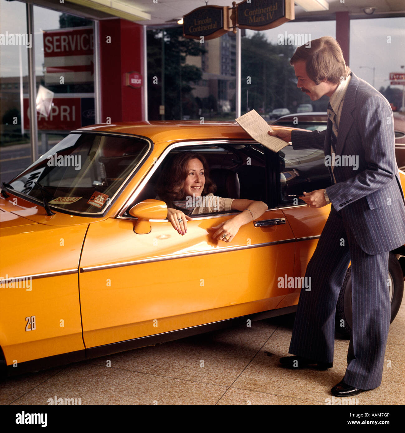 1970 1970s WOMAN SITTING DRIVERS SEAT ORANGE CAR BUY NEW AUTOMOBILE SALESMAN DEALER DEALERSHIP SHOWROOM TEST DRIVE Stock Photo