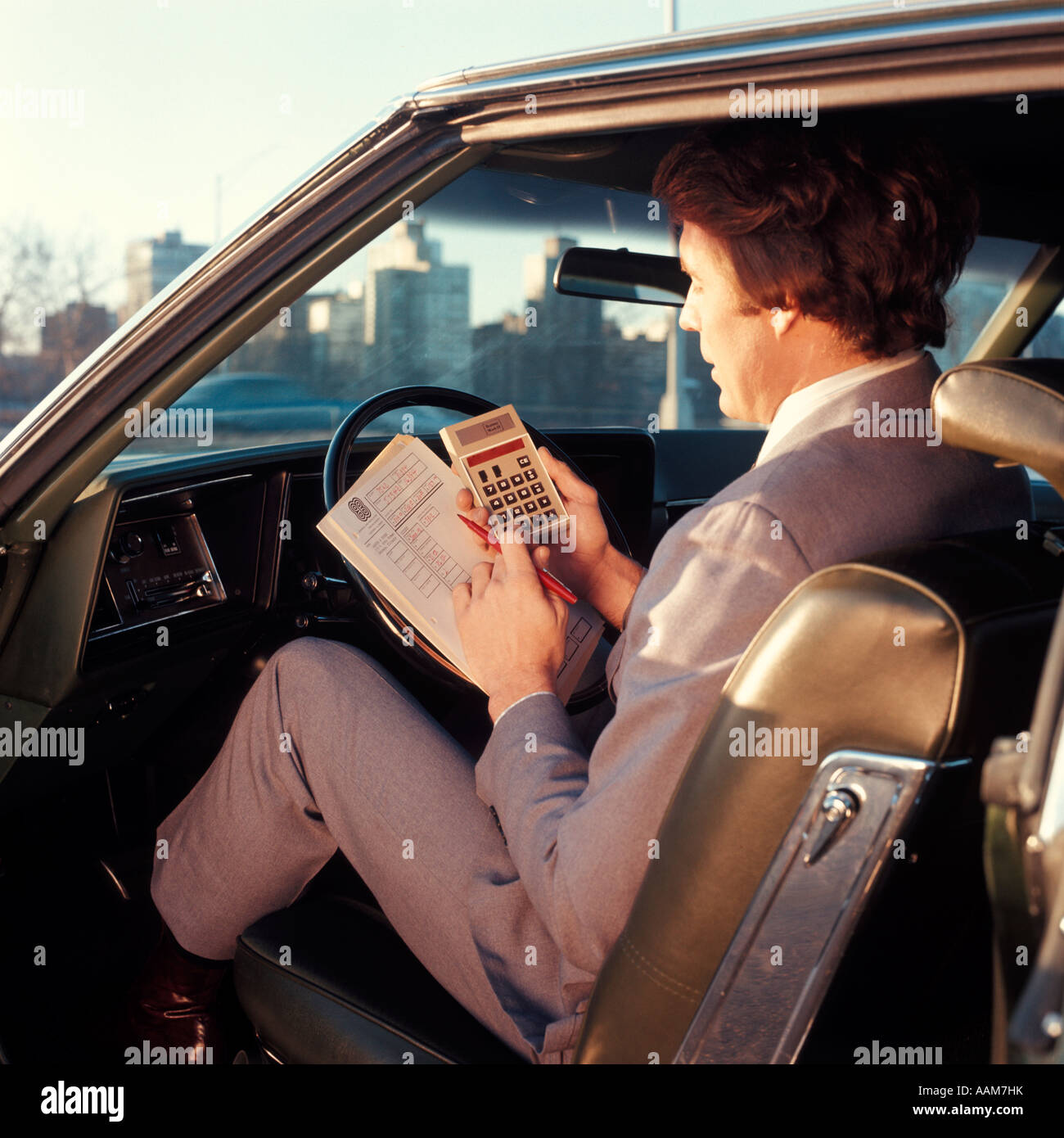 1970 1970s MAN BUSINESSMAN SALESMAN SITTING DRIVERS SEAT CAR DOOR OPEN HOLD PAPERS CALCULATOR BUSINESS CARS Stock Photo