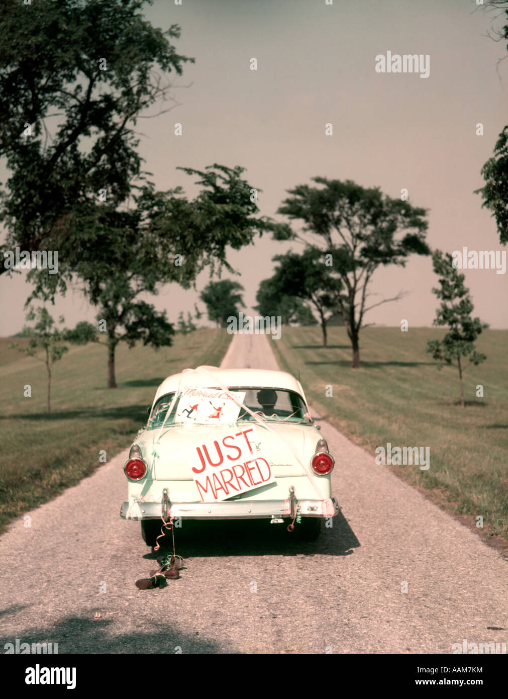 1950s COUPLE BRIDE AND GROOM RIDING IN FORD SEDAN ON BEGINNING OF LONG ROAD JUST MARRIED SIGN AMERICANA NOSTALGIA Stock Photo