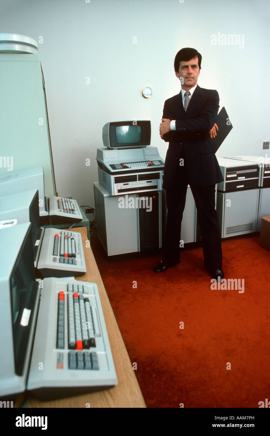 1980s RETRO MAN COMPUTER PROGRAMMER STANDING IN A ROOM WITH EARLY TEXAS INSTRUMENTS HARDWARE SCREENS KEYBOARDS Stock Photo