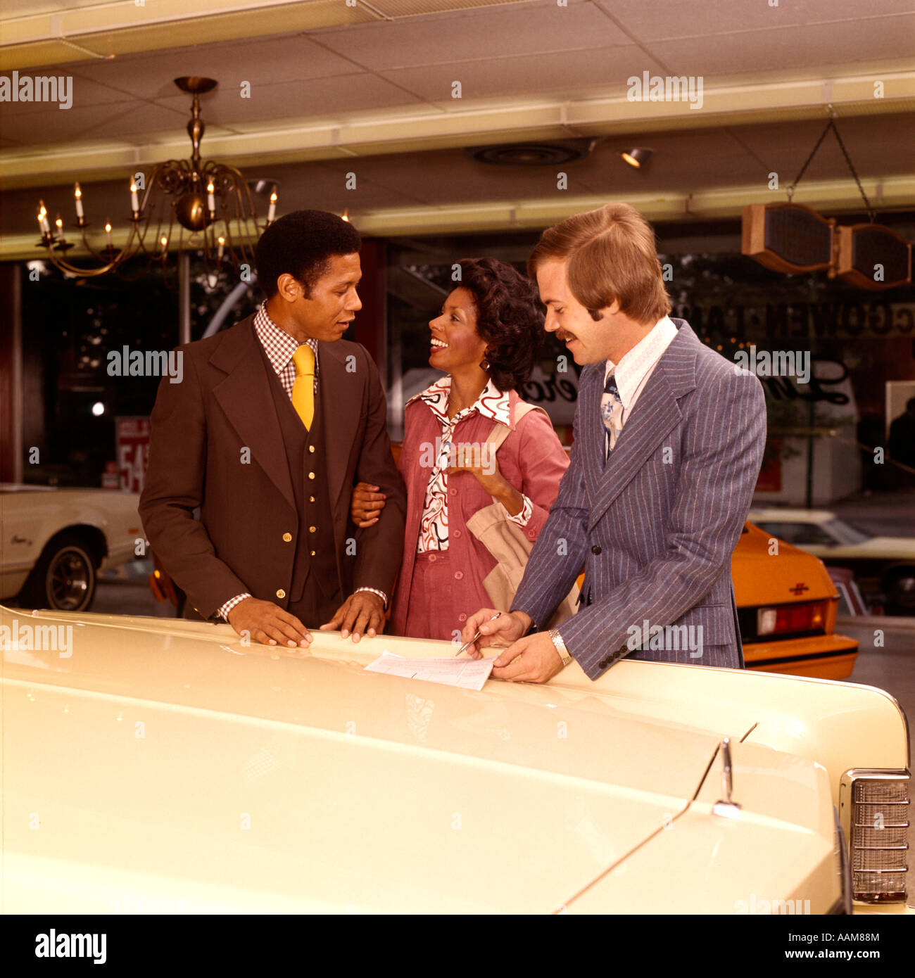1970 1970s AFRICAN-AMERICAN COUPLE MAN WOMAN BUYING NEW CAR WITH SALESMAN DEALER AUTOMOBILE SHOWROOM Stock Photo