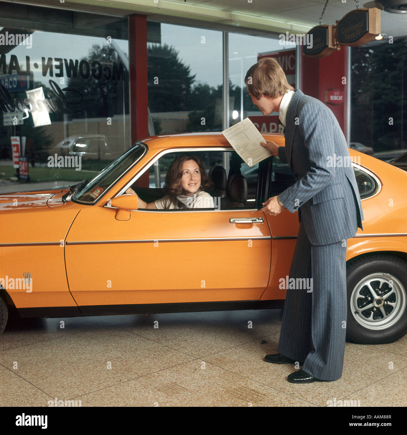 WOMAN DRIVING ORANGE CAR GETTING SERVICE FROM MAN IN BUSINESS SUIT HELP TALKING Stock Photo