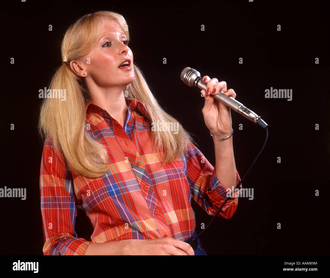 1970 1970s BLOND BLONDE WOMAN PIGTAILS LONG HAIR MICROPHONE PLAID SHIRT SINGER SINGER SINGING FOLK MUSIC ENTERTAINER Stock Photo