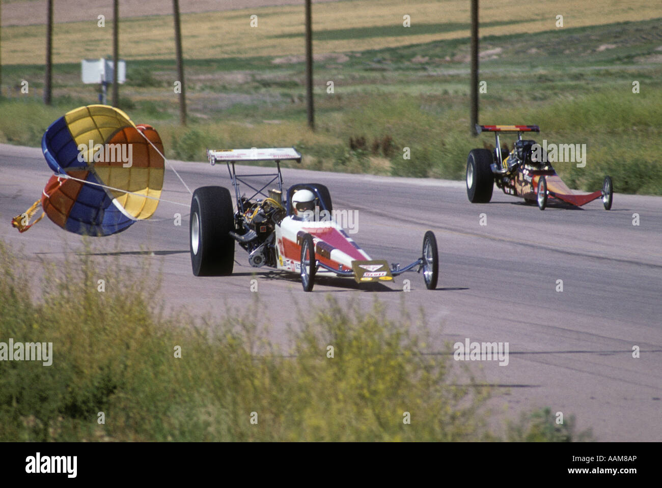 1970s DRAG RACE TWO ALCOHOL BURNING CARS DRAGSTERS ON STRIP NEAR FINISH OPEN DROGUE PARACHUTE RACING SPEED SLOW DOWN Stock Photo