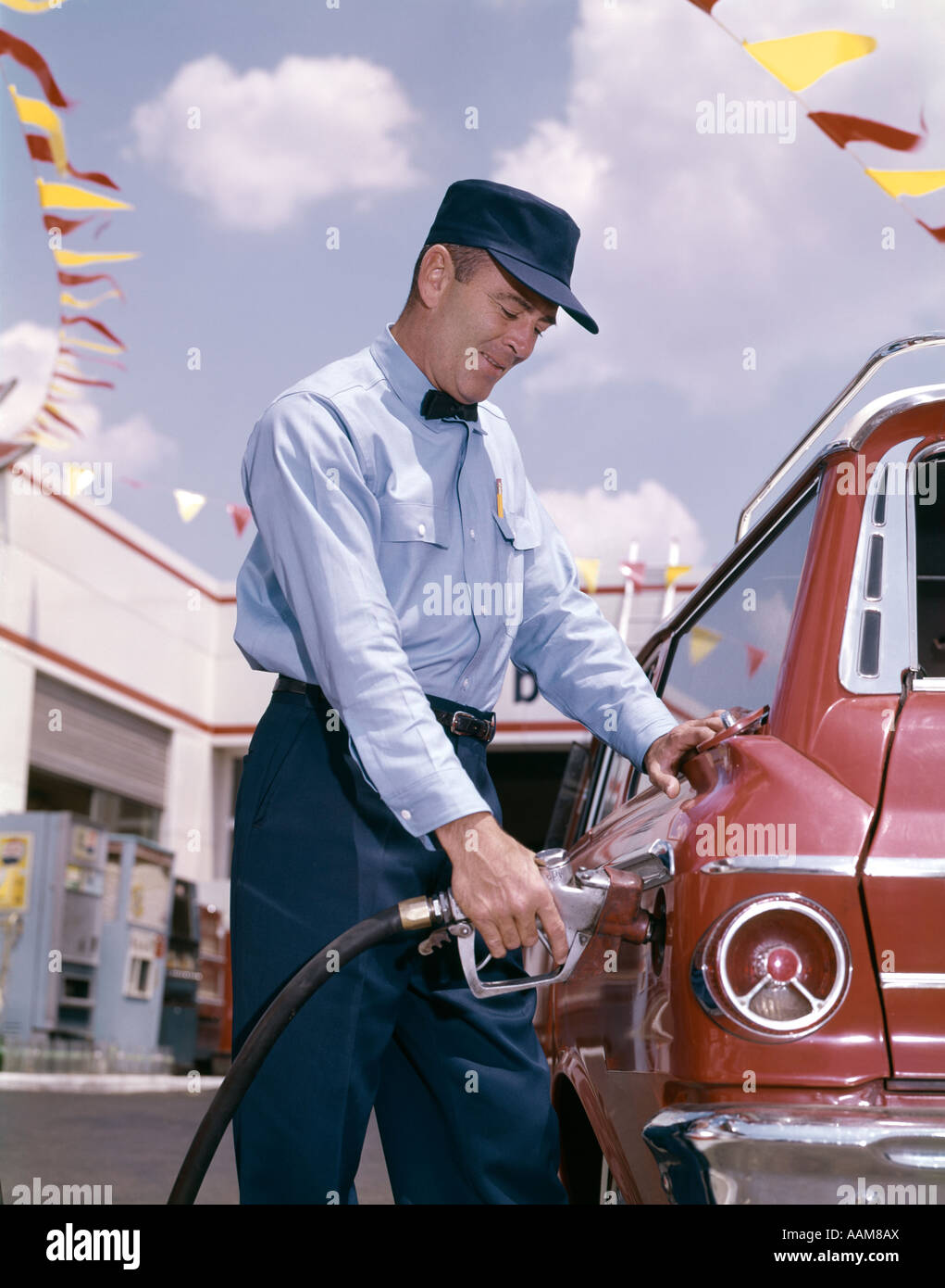 1960s SERVICE STATION ATTENDANT WITH PUMP HOSE FILLING GAS TANK OF AUTOMOBILE Stock Photo