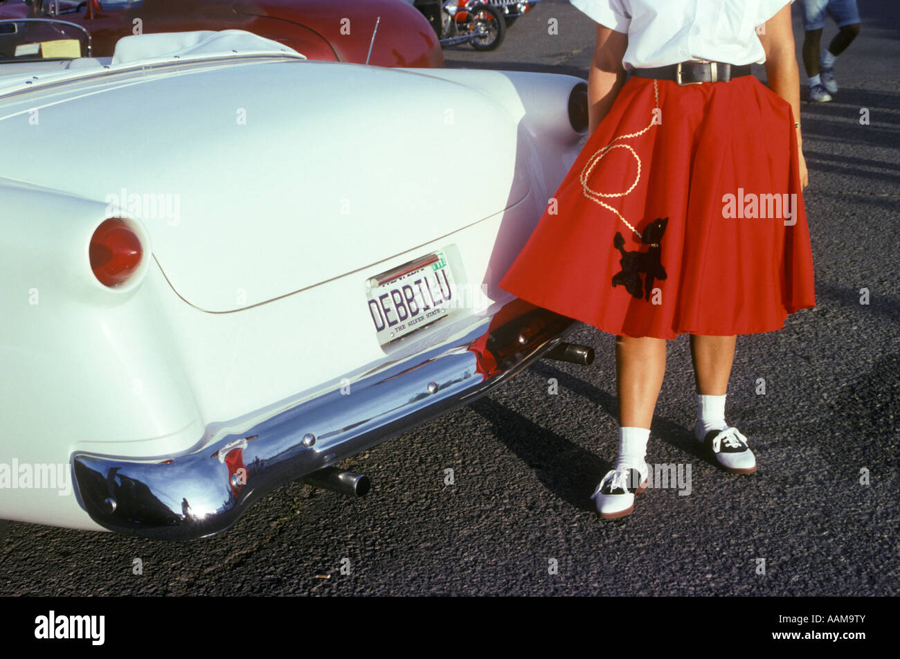 WOMAN IN RED POODLE SKIRT AND SADDLE SHOES NEXT TO WHITE 1950s CAR Stock Photo